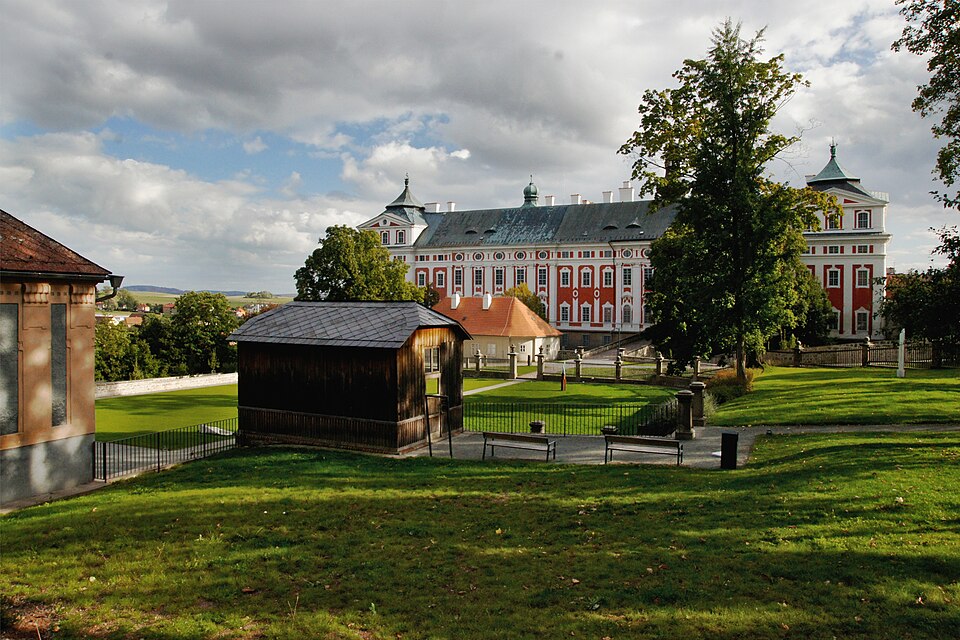 Panoramiczne ujęcie czerwono-białego klasztoru, z ogrodem i zielenią na pierwszym planie.